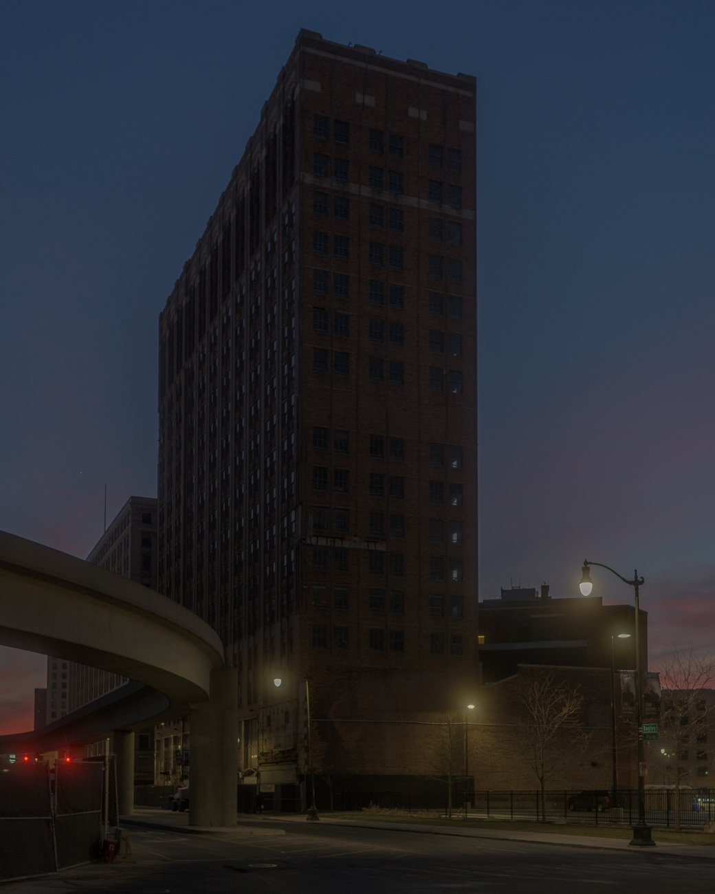 Tall brick building at dusk beside a curved ramp and streetlights.