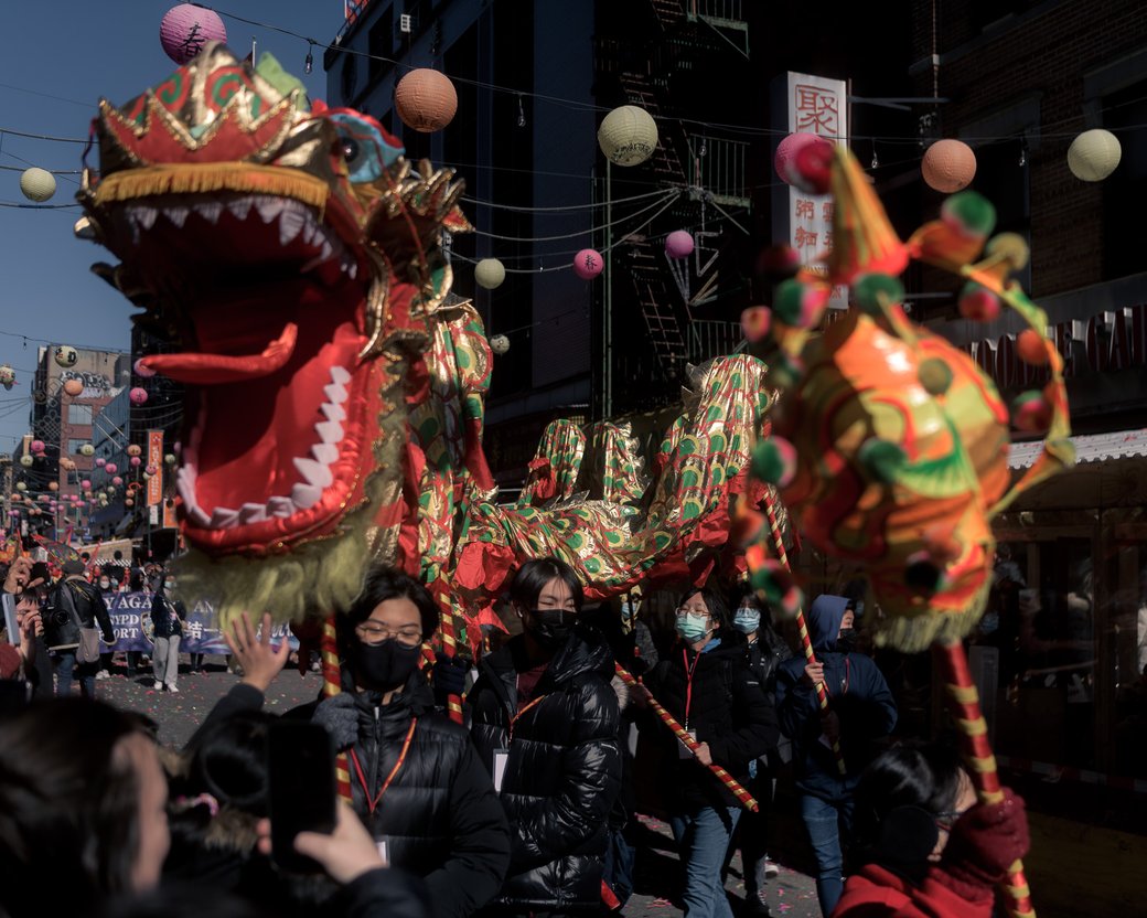 Dragon dance costume weaving through a street parade under hanging lanterns.