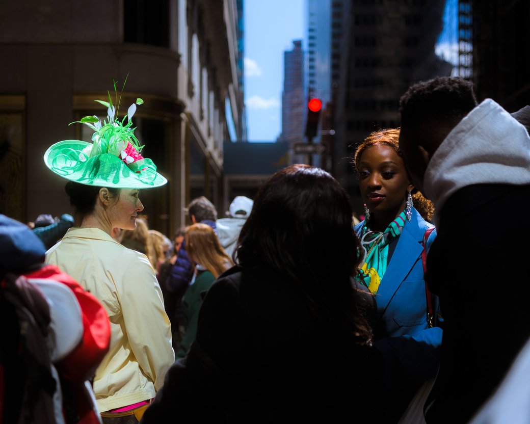 Crowd on a city street with a person in a bright green hat and another in a blue coat.