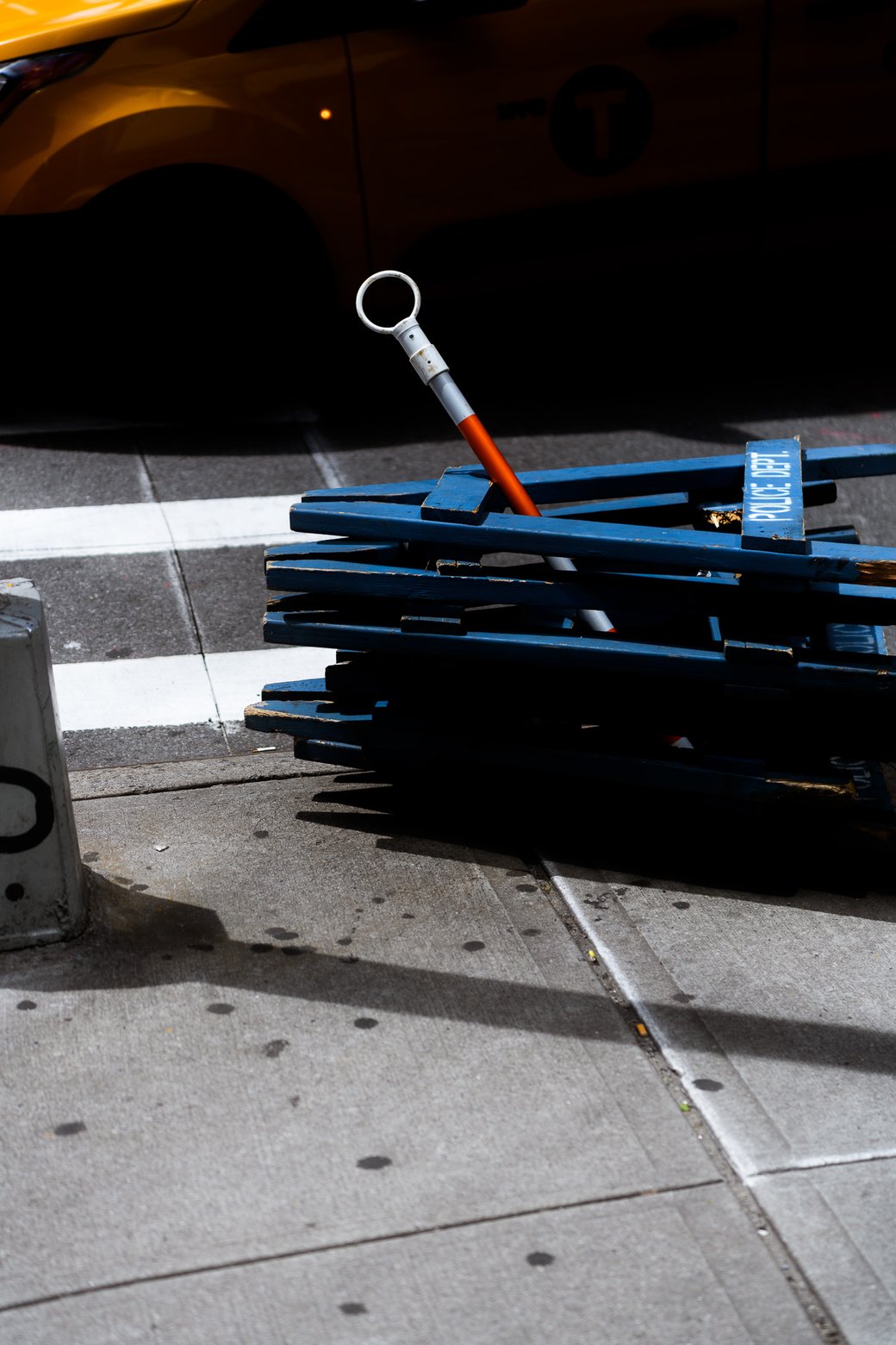 Toppled blue street barricade on a sidewalk with an orange handle and a taxi in the background.