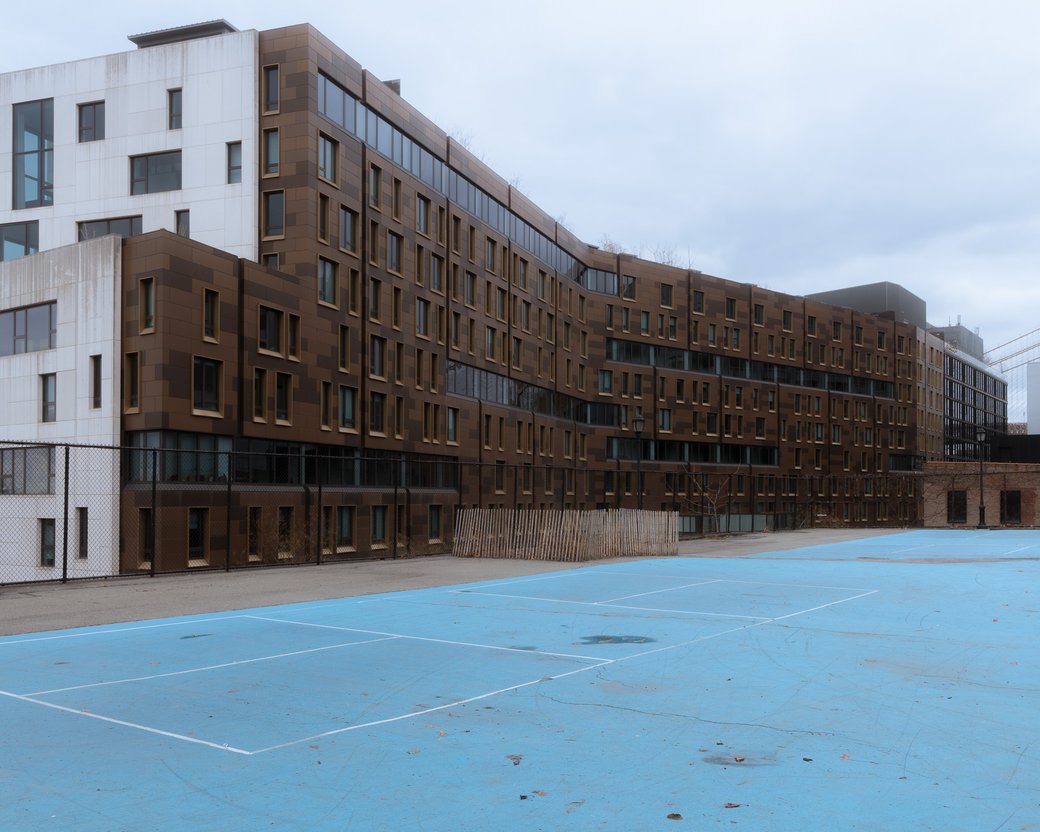 Blue outdoor courts in front of a long brick-and-glass apartment building on a cloudy day.